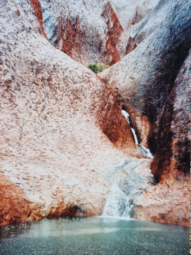 Rain is very rare in the Australian desert. But when it does rain, it makes the rock transform in front of your eyes. I think we had one or two days in a row of actual, decent rain in the half a year I was there. I recall the tourists who had flown in specifically to see Uluru were, for the most part, disappointed.They had in their mind the pictures they’d seen over and over again of a bright red rock, surrounded by red sand, with a bright blue sky as the backdrop. But a couple of smart ones realised that rain was something special when they saw the locals going out of their way to grab their huge cameras and drive the 30+ minutes out to Uluru.This photo is of the same spot as the photo directly above it. The rain makes the rock show its many colours, it gives it a shiny sheen, and it fills all those watering holes. Not to mention showing off what its waterfalls actually look like with water running down them!